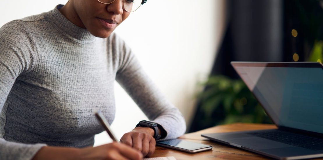 Investor writing in planner in front of laptop.